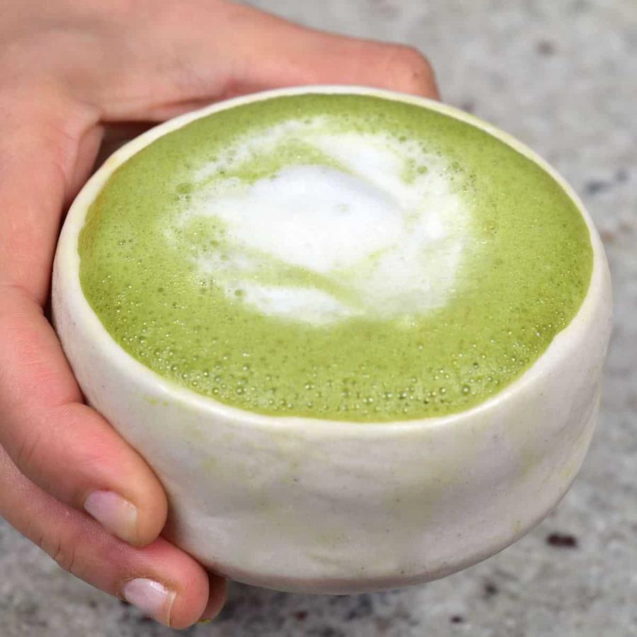 Matcha-Latte - CERES Fair Food A hand holding a green, frothy matcha latte