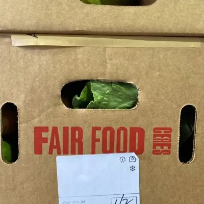FF-side-of-box-closeup - CERES Fair Food Close up of a carboard box from Fair Food, with the vegetable delivery showing through the gaps and the logo printed in red.