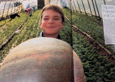 Chris_Book_polytunnel - CERES Fair Food A magazine photo of a child smiling in a polytunnel, holding a large pumpkin