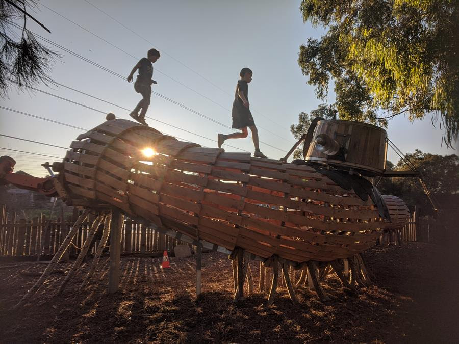 Terra Wonder Playspace CERES Millipede Playground at sunset with young people running across the sculpture