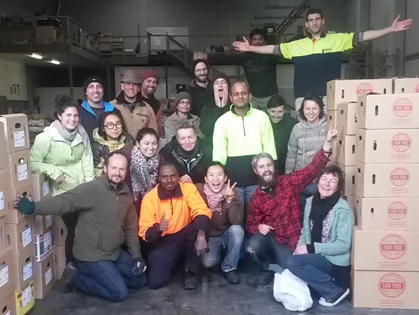 K - CERES Fair Food Group of volunteers posing in a warehouse with stacked cardboard boxes labeled Fair Food.