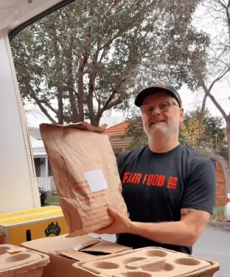 Delivery driver Chop, standing by an open delivery van and holding a returnable sustainable insulated bag.